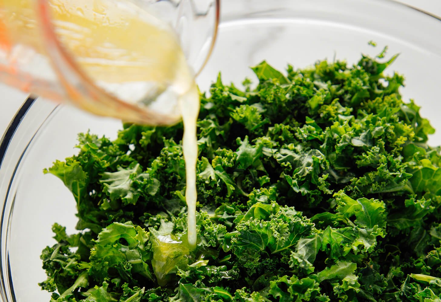 drizzling dressing over kale salad